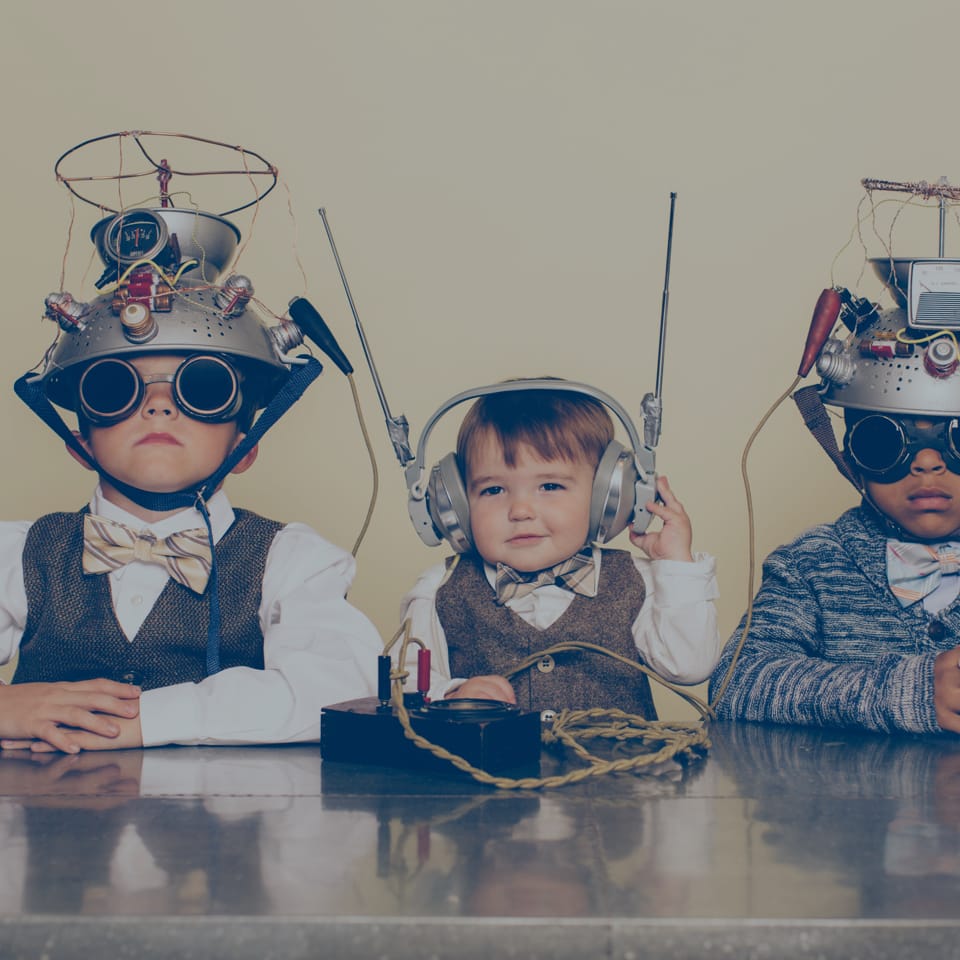 Three children are seated and wearing retro-style makeshift "thinking caps" featuring various wire and antenna attachments. One child wears large headphones, and they all have serious expressions, dressed in formal attire with bow ties.