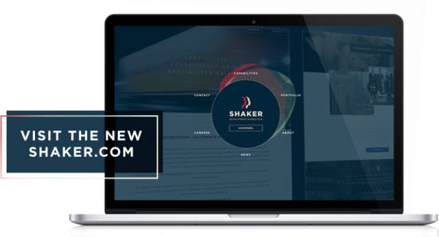 A laptop screen displays a website with a central circular logo labeled "Shaker." To the left of the laptop, there is a dark rectangular banner with white text that reads, "Visit the new Shaker.com.