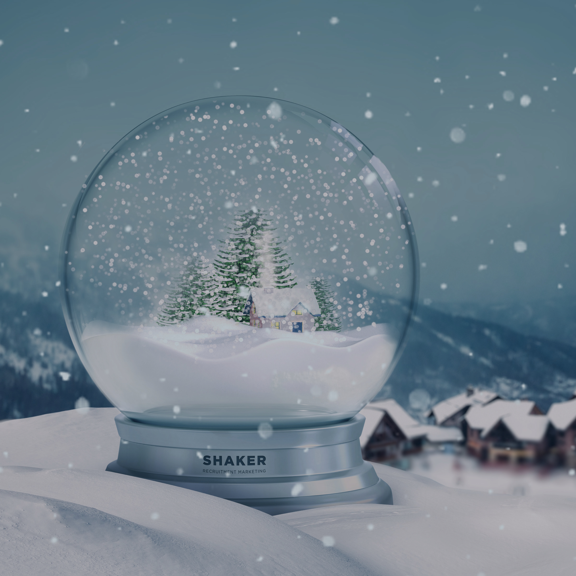 A snow globe sits on a snowy ledge, featuring a small cabin surrounded by evergreen trees. Snowflakes gently fall inside the globe, while a snowy mountain village is visible in the background under a cloudy, wintry sky. The base of the snow globe is labeled "SHAKER.