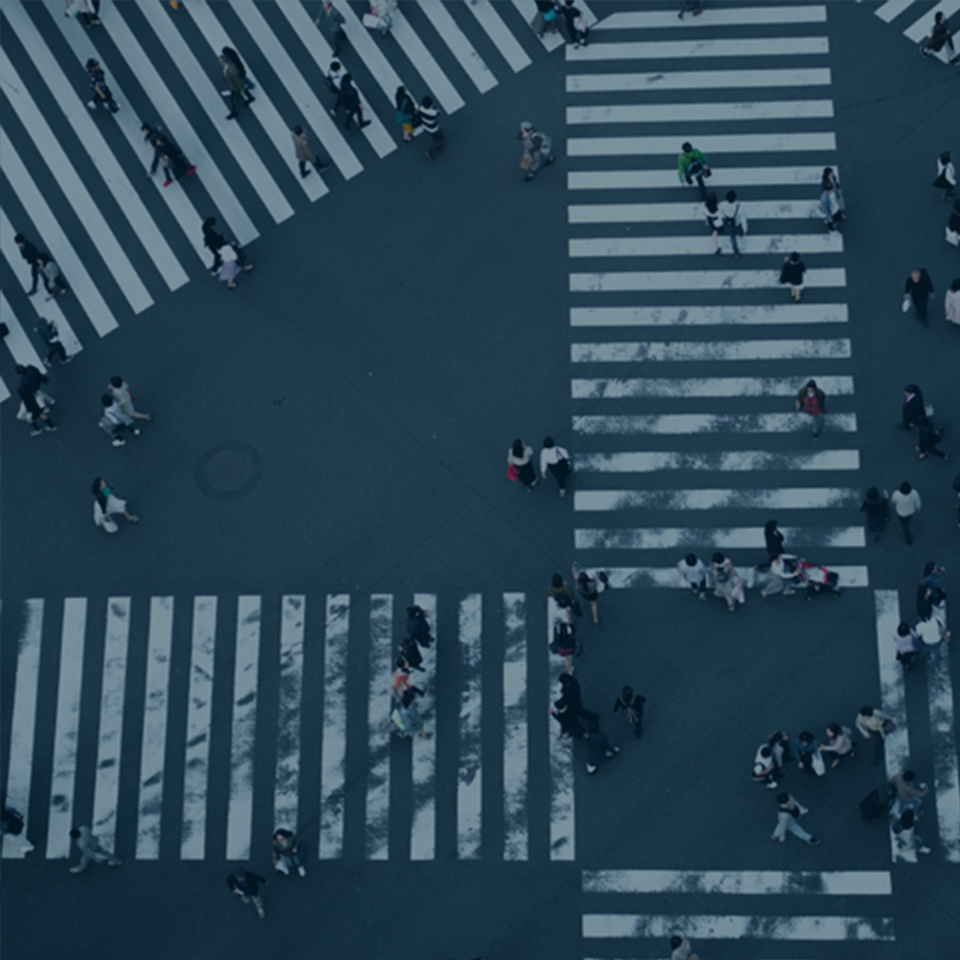 Aerial view of a busy crosswalk intersection with multiple lanes of white zebra stripes. Pedestrians are crossing in various directions, creating a bustling atmosphere reminiscent of the ever-changing job market. The scene captures the organized chaos of urban life.