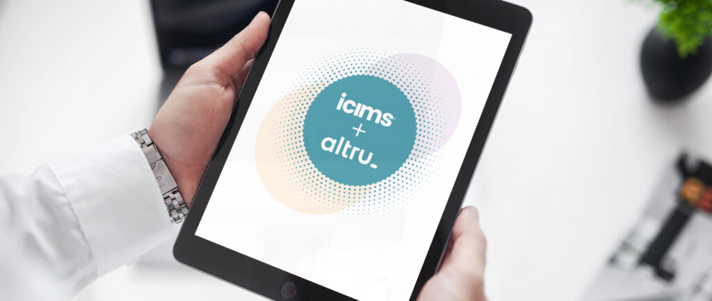 A person holds a tablet displaying a circular graphic with two intersecting circles. One circle contains the text "icims" and the other "altru." The image suggests a combination or partnership between these two entities.