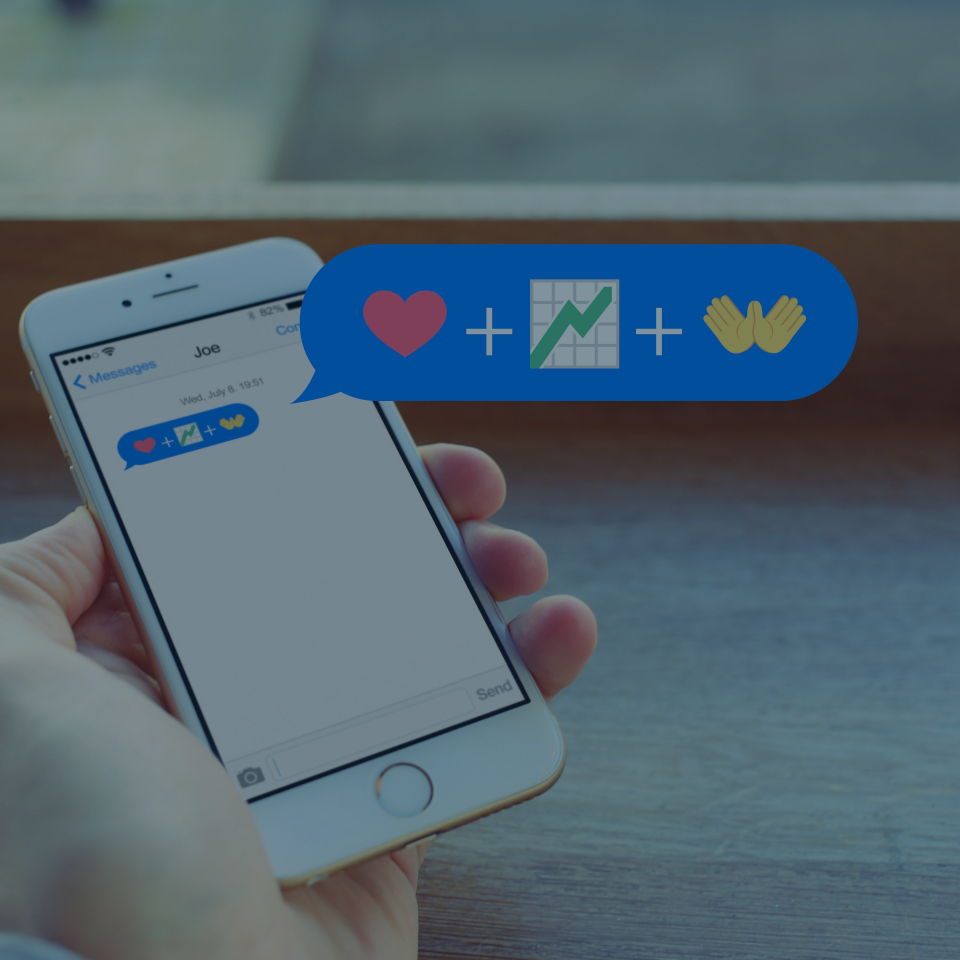A person holding a smartphone, which displays a text message containing three emojis: a red heart, an increasing green graph, and two raised hands. A blue message bubble above the phone shows the same emojis in a larger format.