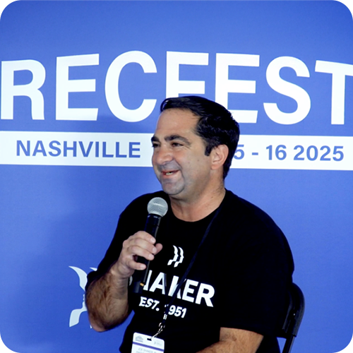 A man holding a microphone sits and smiles in front of a blue backdrop that reads "RECFEST NASHVILLE 15-16 2025." He wears a black t-shirt and a lanyard.