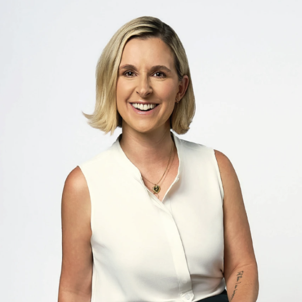 A woman with blonde hair smiling at the camera, wearing a white sleeveless collared shirt and a gold necklace.