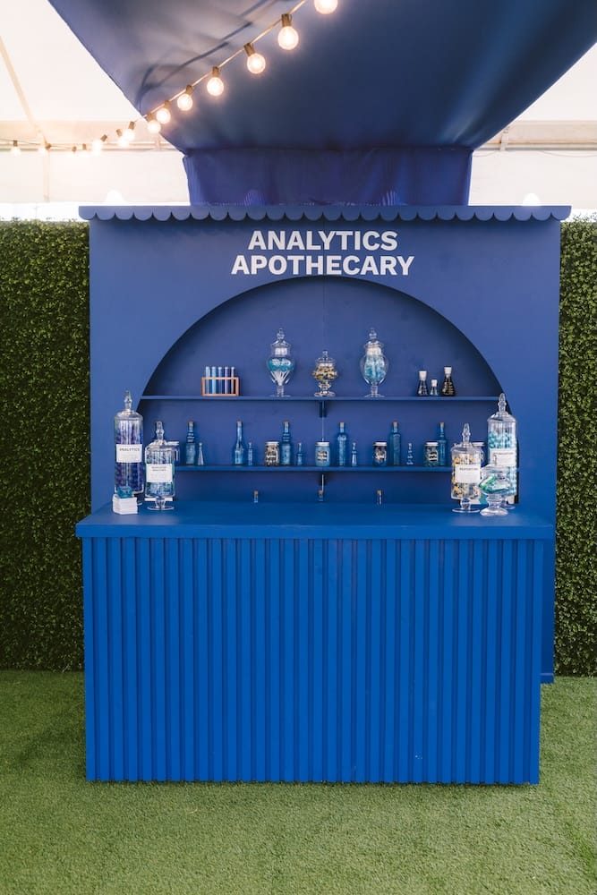 A blue “Analytics Apothecary” booth featuring shelves of assorted glass bottles and apothecary jars.