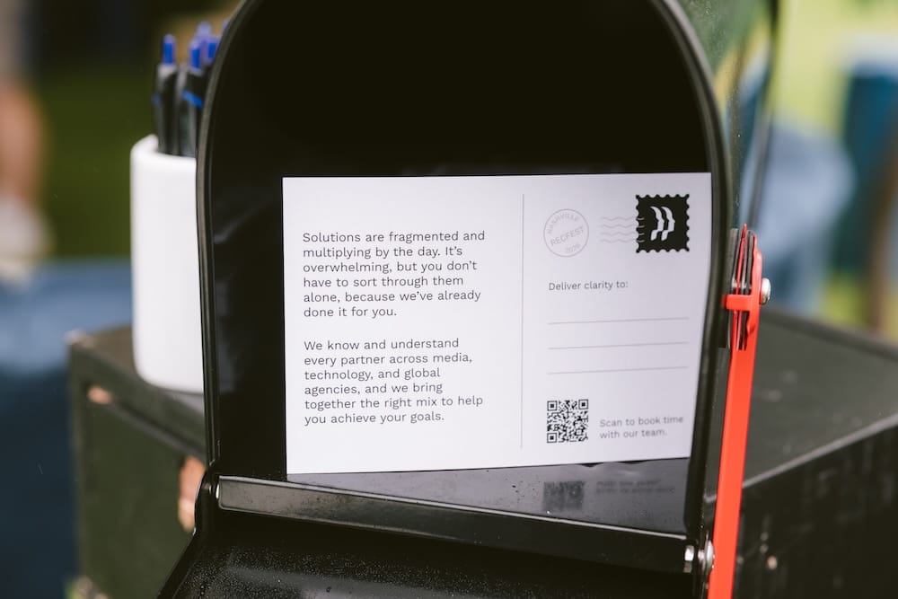 A postcard inside a black mailbox that reads, “Solutions are fragmented and multiplying by the day,” with a QR code and text prompting to “Scan to book time with our team.”
