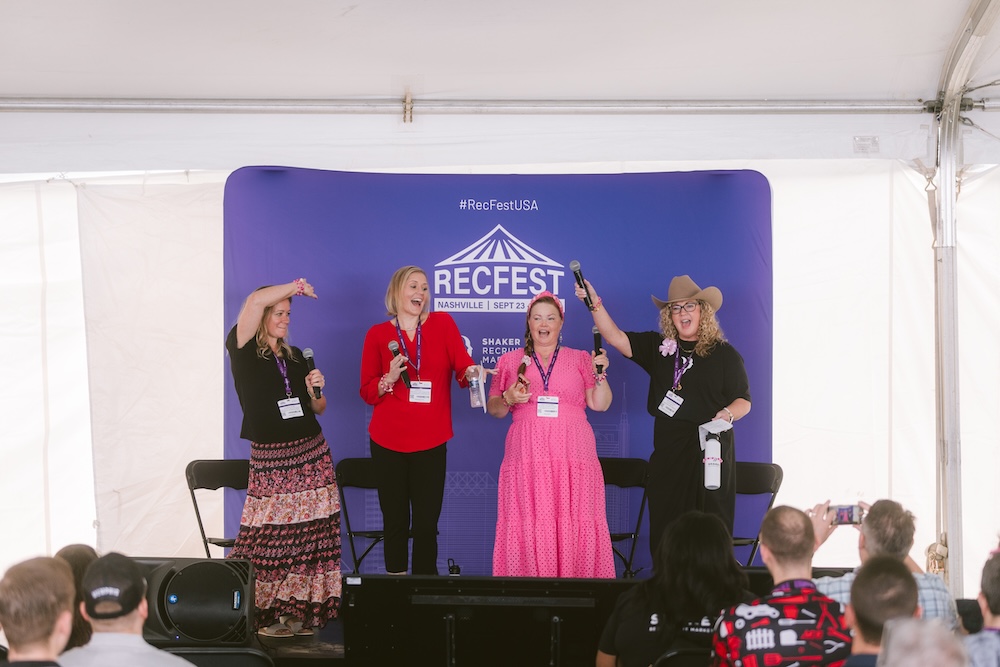 Four women speaking into microphones on a stage in front of a branded RecFest Nashville backdrop, facing an audience.