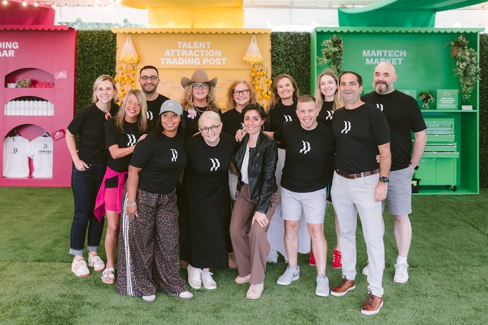A group of thirteen people standing together in front of three colorful, branded event booths.