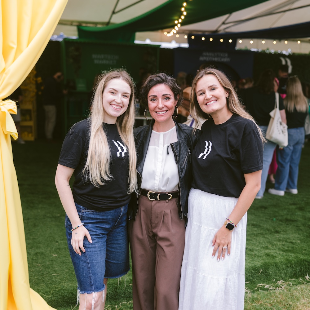 Three women posing for a photo under a tent at an event.